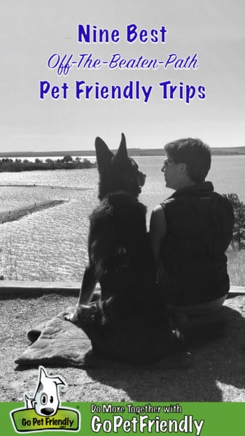 Black and white photo of a woman and a German Shepherd Dog sitting together on a bluff overlooking a lake smiling at each other